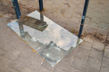 The shattered glass pane of a public transport stop lying on the ground.