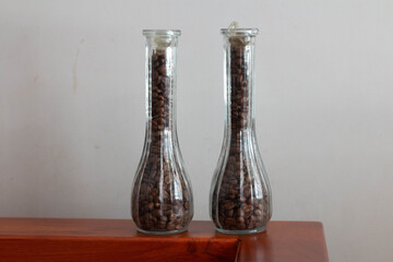 Two bottles filled with coffee beans placed on wooden furniture 