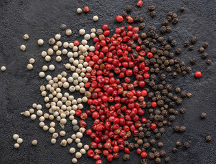 White, pink and black peppercorns in bulk on a black textured background. Spices and herbs.
