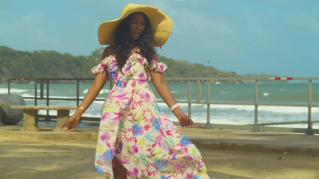 A young woman in a flower dress dancing and singing with rough waves from the ocean in the background