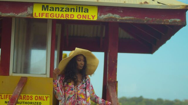 A girl stands at a lifeguard booth in a straw hat and a sexy bikini