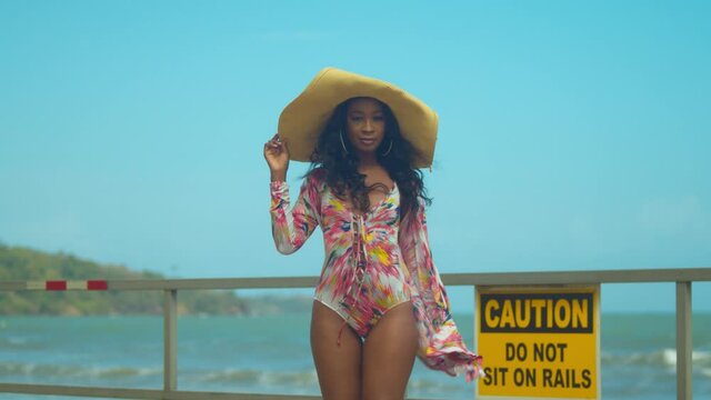 Sexy girl walks on a boardwalk in a bikini with mountains and ocean waves crashing in the background