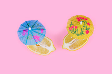 Lemon cut in half with cocktail umbrellas on pastel pink background. Summer food concept.