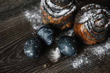 easter cake with poppy seeds in powdered sugar on a wooden table top with blue-painted eggs