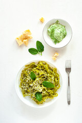 Green noodles with spinach and parmesan cheese in a white plate on a white table. Basic ingredients. Healthy food. View from above. Vertical photo.