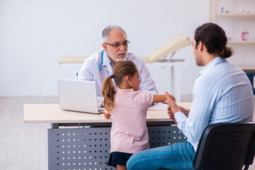 Fototapeta premium Small girl with her father visiting old male doctor