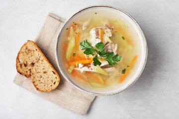 chicken soup in a bowl on a gray table with a piece of bread, top view, close-up