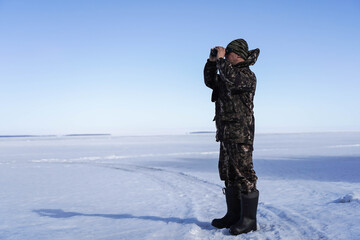 Naklejka premium a man in a military uniform looks through binoculars against a background of a winter landscape