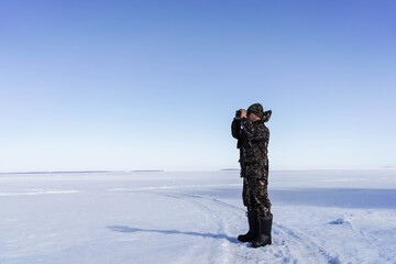 Fototapeta na wymiar a man in a military uniform looks through binoculars against a background of blue sky and winter landscape