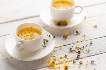 two cups of aromatic flower tea, soothing, medicinal on white wooden background