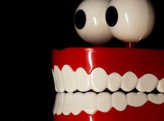 A smiling toy prosthesis, with white teeth and large eyes isolated against a black background.