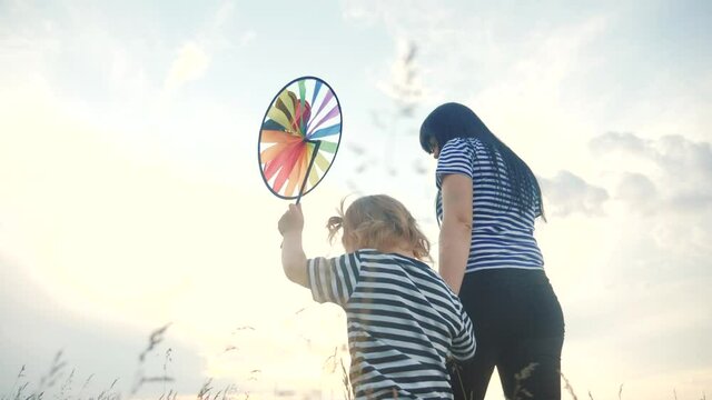 people in the park. happy family together mom and daughter are walking with play pinwheel a wind toy. happy family concept. child and mother plays with lifestyle windmill. girl kid blonde and parent