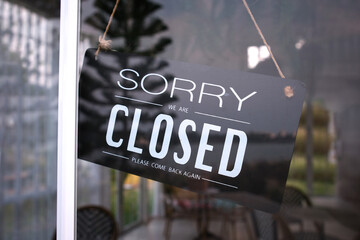 Sorry we are closed sign board through the glass of coffee shop or restaurant . 