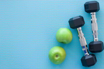 Empty space for the text. Two green apples and dumbbells lie on the sports mat. Top view.