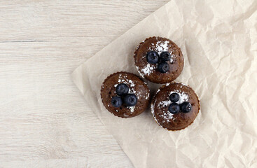 Chocolate muffins with blueberries on baking paper on wooden background