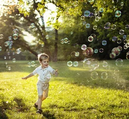 Poster Cute little boy chasing soap bubbles © konradbak