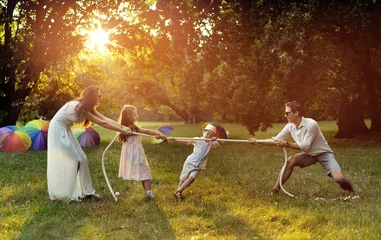 Foto op Aluminium Joyful family playing tug-of-war in the park © konradbak
