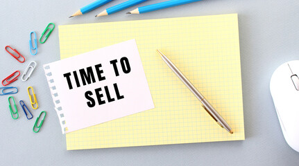TIME TO SELL is written on a piece of paper that lies on a notebook next to office supplies.