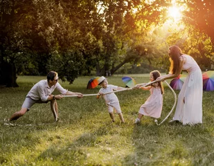 Foto op Canvas Joyful family playing tug-of-war in the park © konradbak