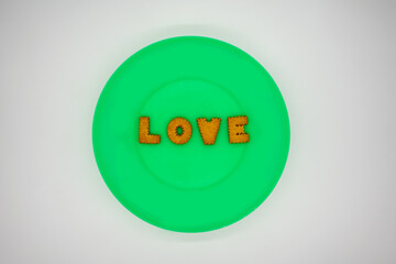 Letter biscuit in order for LOVE on green plastic plate or dish isolated on white background.