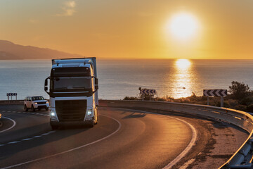 Truck with refrigerated semi-trailer on a mountain road with the sea and the sun on the horizon.