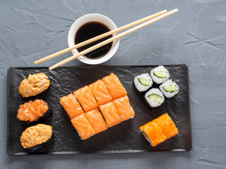 a variety of rolls and sushi gunkan nested on a black plate. next to it are bamboo wasabi sticks and sauce. Top view, flat lay. traditional Japanese cuisine