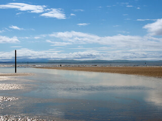 clouds reflected in the water during sn incoming tide on crosby beach in merseyside with a blue sunlit sky