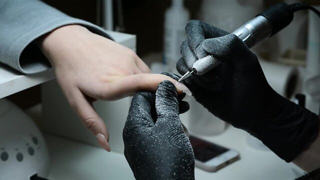 the master of manicure and pedicure removes gel polish from the nail. close-up manicure. nail extensions. the manicurist works with a milling cutter. nails on the contour light. Removing the material