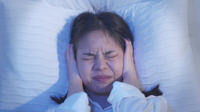 Young Asian woman sleeps in bed are stressed, annoyed, suffer from loud noises, headaches and irritability and use pillows to cover their ears.