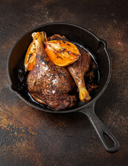 Slow cooked duck legs with orange wedges in cast iron skillet frying pan