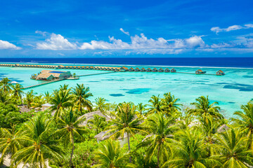 Tropical island paradise with white sandy beach shore, seaside and summer palm trees with sea horizon and luxury water villas, bungalows. Drone aerial view over Maldives islands. Sunny summer vacation