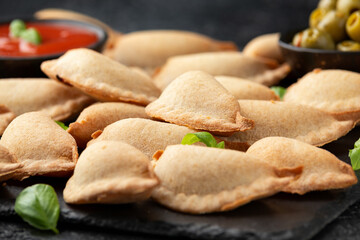 Margarita Margherita pizza parcels pockets filled with tomato, mozzarella cheese and basil served on black slate board with marinara sauce and olives. Party finger food
