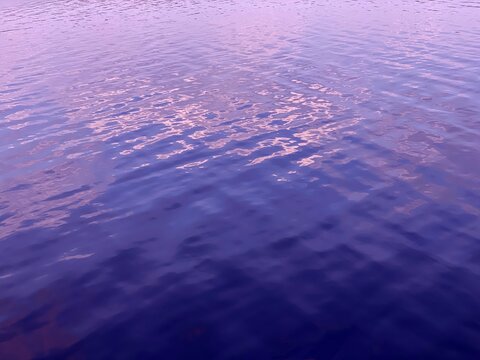 Purple blue rippled shiny water in calm river background.