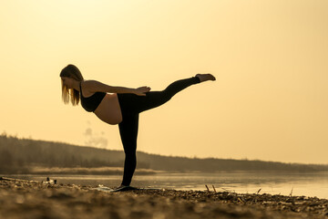 Happy pregnant woman doing yoga at a lake at a beautiful sunset