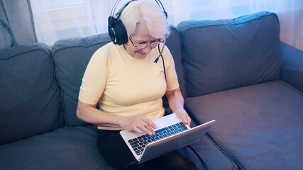 Elderly woman with headset having video call with family and waving to camera. Old people and technology. High quality photo