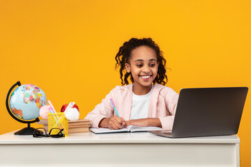 Portrait of smiling black girl sitting at table and writing