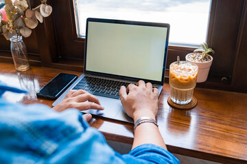 Close-up of male hands using laptop and smartphone at coffee shop with white mockup screen, man's hands typing on laptop keyboard, side view of a man using computer in cafe