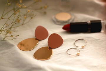 Various make up products, earrings, rings and flowers on white background. Selective focus.