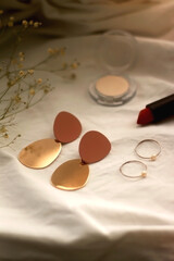 Various make up products, earrings, rings and flowers on white background. Selective focus.