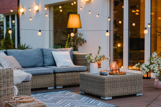 Summer evening on the terrace of beautiful suburban house with patio with wicker furniture and lights
