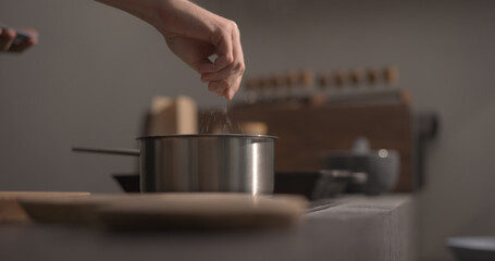 man hand salting bopiling water for pasta in saucepan closeup
