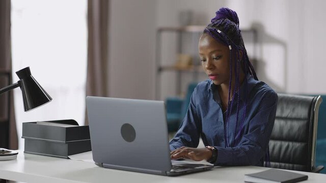 afro-american woman is working with laptop, remote job at home, young lady is sitting at table and sending email