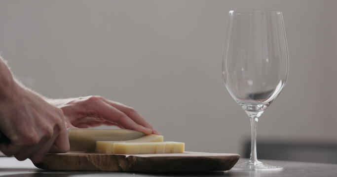 man hands cutting vintage cheese on oliveboard with wine glass