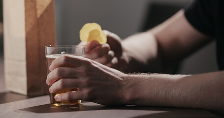 Man drinking amber color fizzy drink with bag of potato chips