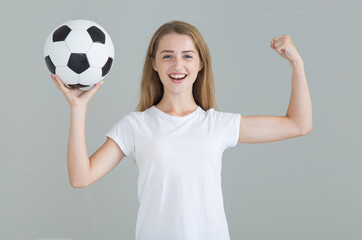 Young athletic woman with a soccer ball looking at the camera. Isolated on a gray background.