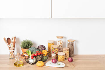 Fototapeta na wymiar Assortment of pasta in glass jars, olive oil, vegetables and kitchen utensils on wooden table. Traditional italian ingredients, healthy balanced food, sustainable lifestyle, zero waste concept.