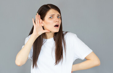 Tell me louder. Portrait of attentive brunette young woman with hairstyle in casual style standing with hand gesture on ear and looking at camera. studio shot isolated on gray background.