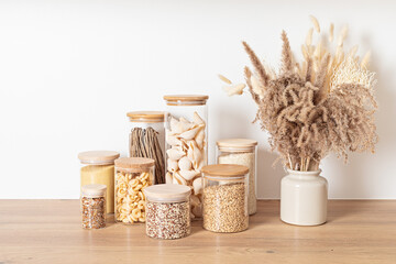 Assortment of grains, cereals and pasta in glass jars and dry herbs on wooden table. Healthy balanced food ingredients, sustainable lifestyle, zero waste storage idea, eco friendly concept.