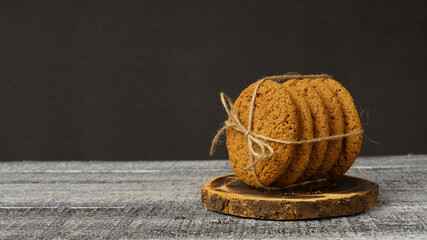 a stack of oatmeal cookies rewound with twine thread lies on a wooden round board on a black and...