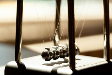 Classic Newtons cradle in sunlight, shallow dof, metal balls still macro, extreme closeup. Momentum, movement physics and common physical laws, simple law of motion abstract concept, nobody